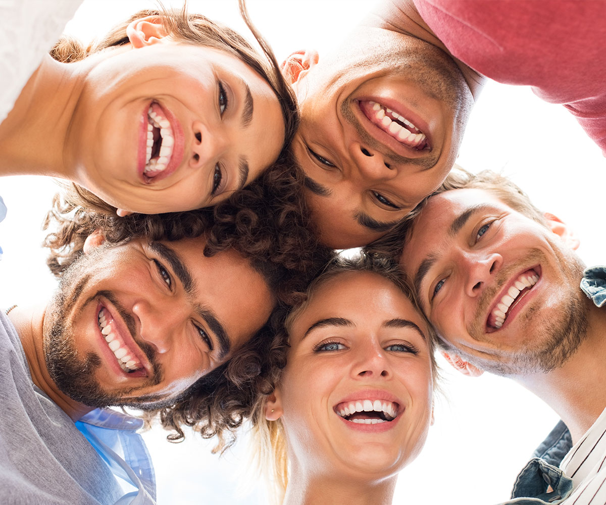 A group of young adults with broad smiles, posing closely together for a cheerful photograph.